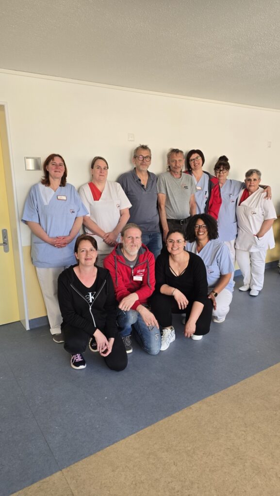 Group of healthcare workers and volunteers posing together in a bright hospital corridor, some in scrubs and name tags.