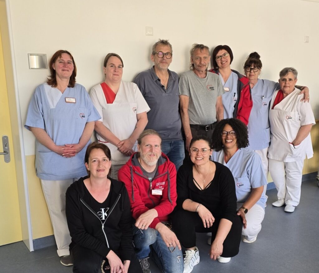 Group of healthcare workers and volunteers posing together in a bright hospital corridor, some in scrubs and name tags.